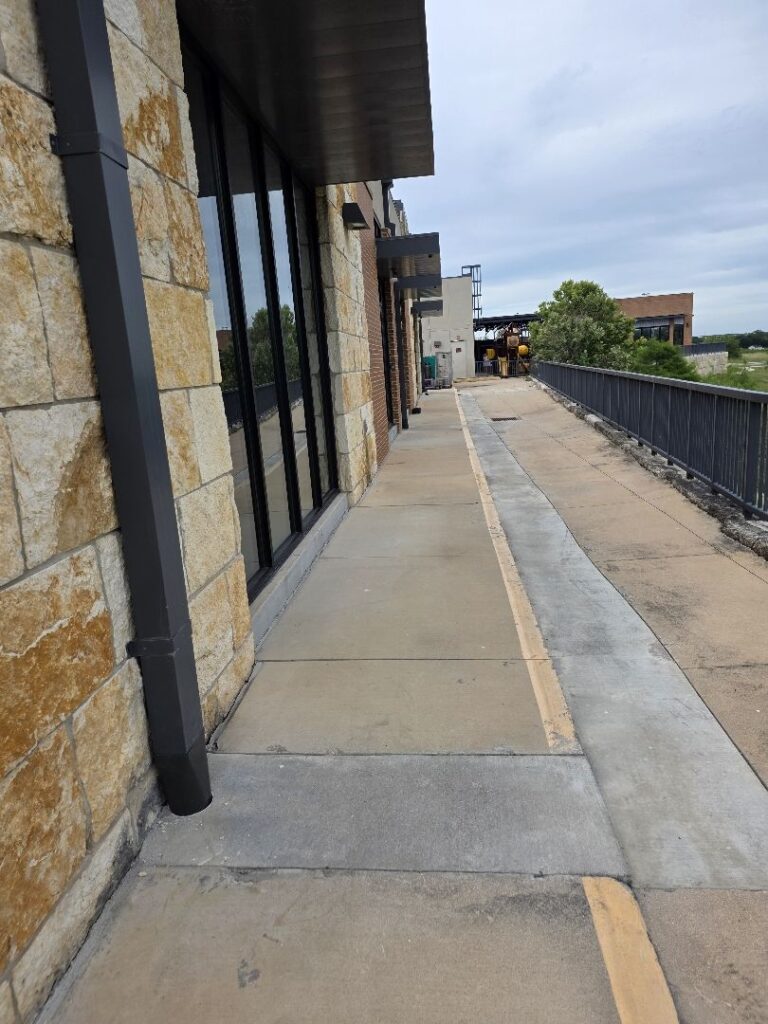 Commercial downspout run down a limestone office building above a trench drain